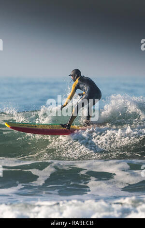 Ein Surfer auf einem longboard auf einer Welle an einem Wintertag. Stockfoto