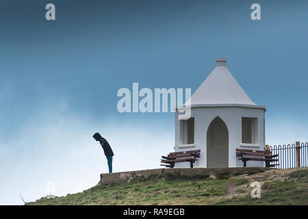 Ein Mann stand neben der alten Küstenwache Lookout Station und lehnte sich in starken Winden auf den Towan Kopf in Newquay in Cornwall. Stockfoto