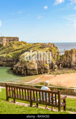TENBY, Pembrokeshire, Wales - AUGUST 2018: Person sitzen auf einer Bank mit Blick auf das Schloss und Strand St Catherine's Insel in Tenby, Wales Stockfoto