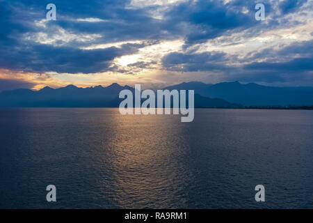 Schönen Sonnenuntergang bewölkten Himmel und dunklen Meer Wasser mit Silhouetten der Berge im Hintergrund. Es kommt die Nacht. Horizontale Farbfotografie. Stockfoto