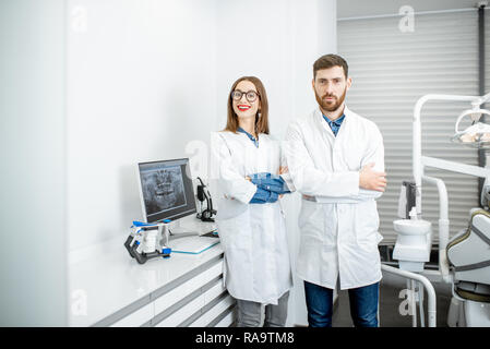 Porträt von einem Zahnarzt mit junge Frau Assistant in Weiß medizinische Kleider stehen in der Zahnarztpraxis Stockfoto