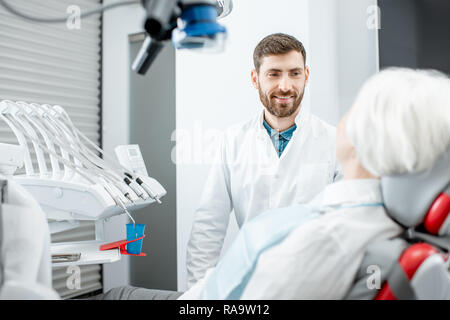 Stattliche Zahnarzt während der Konsultation mit älteren Frau, die in der Zahnarztpraxis Stockfoto