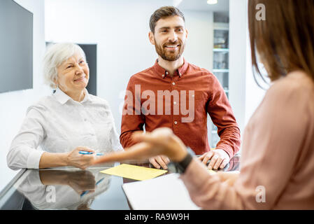 Lächelnder Mann mit seiner älteren Mutter im Gespräch mit der Rezeption im Krankenhaus Stockfoto