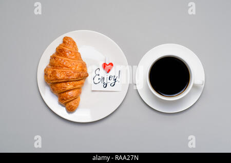 Frisch gebackene Croissants, Tasse Kaffee und genießen Sie Hinweis auf grauem Hintergrund, Frühstück Konzept, Ansicht von oben Stockfoto