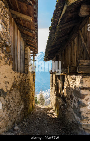 Schmale Gasse zwischen den alten Häusern mit Bergblick in Castello, eine kleine Stadt in der Region Val di Sole, Gemeinde Pellizzano, Trient, Trentino, Italien Stockfoto