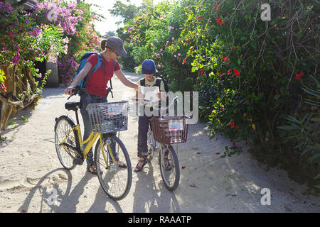 Mutter und Sohn mit dem Fahrrad Lesen einer Karte erkunden traditionellen Dorf Taketomi auf Straßen mit Hibiskus Insel in Okinawa, Japan abgedeckt Stockfoto