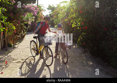 Mutter und Sohn mit dem Fahrrad Lesen einer Karte erkunden traditionellen Dorf Taketomi auf Straßen mit Hibiskus Insel in Okinawa, Japan abgedeckt Stockfoto