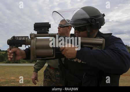 Us Marine Gunnery Sgt. William Radebaugh, nicht-tödliche Waffen Instructor, Uhren als Satoshi Kinjo, japanisch Security Guard, Torii, der M32 Granatwerfer schießt während einer Non-Lethal Waffen Instructor Kurs an Bord Camp Hansen, Okinawa, Japan, Jan. 17, 2017. Der Kurs vermittelt Personal die korrekten Techniken bei der Durchführung von Taser Ausbildung, oleoresin Capsaicin Exposition und riot control Team Taktik. Stockfoto