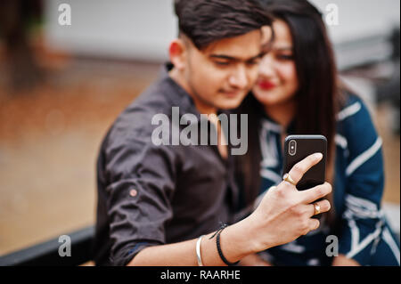 Indische Paar stellte im Freien, auf der Bank sitzen zusammen und suchen am Handy, so dass selfie. Stockfoto