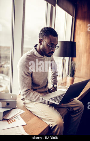 Ernsthafte brünett Mann an seinem Laptop starrend Stockfoto