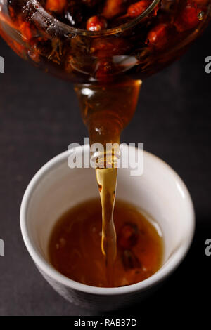 Der Prozess der Zubereitung von Kaffee. Teezeremonie, einer Tasse frisch Briar, eine dunkle Stimmung. Heißes Wasser aus dem Wasserkocher in die Schale mit den Hüften gegossen. Close-u Stockfoto