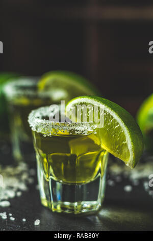 Mexikanische Gold Tequila shot mit Kalk und Salz auf schwarzen Stein Tischfläche, selektiver Fokus, flacher Tiefe des Feldes, kopieren. Stockfoto