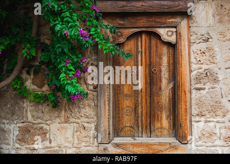 Schöne hölzerne geschlossene Fenster in der Mauer des alten Hauses und Grüner Baum mit lila Blüten wachsen in der Nähe von Es. Horizontale Farbfotografie. Stockfoto