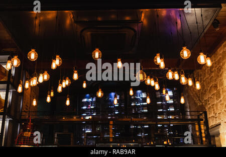 Viele elektrische Lampen Lampen hängen von der Decke im Restaurant innen und leuchten in der Dunkelheit. Der dunkle Hintergrund. Horizontale Farbfotografie. Stockfoto