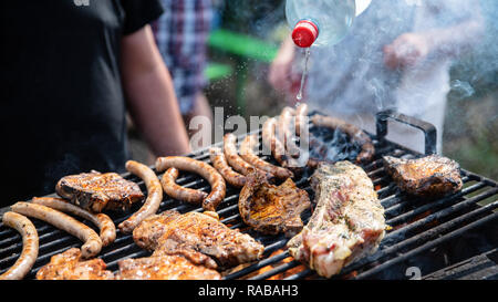 Spareribs und Fleisch, Würstchen auf dem Grill. Prozess des Kochens, wodurch sich die Flammen mit Wasser aus der Flasche. Freunde haben einen schönen Rest. Stockfoto