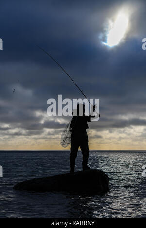 Vitt, Deutschland. 30 Dez, 2018. Ein Angler steht mit einem sich drehenden Stange auf einem Stein in der Ostsee in der Nähe des Fischerdorf Vitt am Kap Arkona. Foto: Patrick Pleul/dpa-Zentralbild/ZB/dpa/Alamy leben Nachrichten Stockfoto