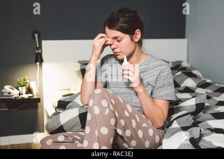 Das Thema saisonale Erkältung, Schnupfen Grippe virus Infektion. Junge kaukasier Frau zu Hause Schlafzimmer Bett verwendet spray Tropfen Medizin an ihre Nase für Sno Stockfoto