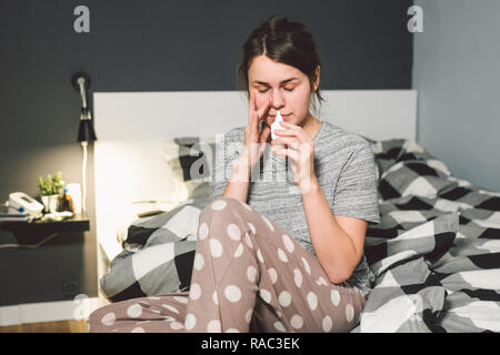 Das Thema saisonale Erkältung, Schnupfen Grippe virus Infektion. Junge kaukasier Frau zu Hause Schlafzimmer Bett verwendet spray Tropfen Medizin an ihre Nase für Sno Stockfoto