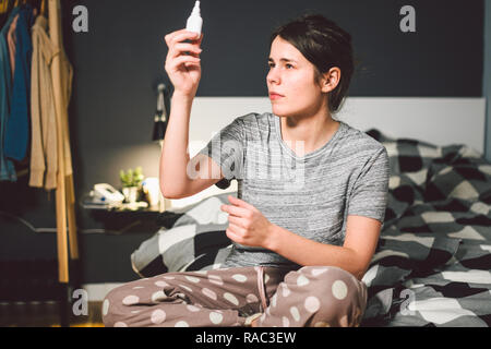 Das Thema saisonale Erkältung, Schnupfen Grippe virus Infektion. Junge kaukasier Frau zu Hause Schlafzimmer Bett verwendet spray Tropfen Medizin an ihre Nase für Sno Stockfoto