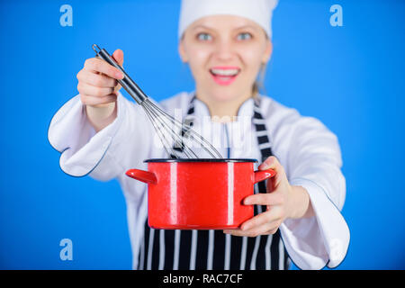 Schlagsahne Tipps und Tricks. Frau Koch halten Schneebesen und Topf. Langsam Rühren, Schlagen oder schlagen Creme beginnen. Spannend wie pro. Mädchen in der Schürze Schlagsahne Eier oder Creme. Mit der Hand schlagen. Stockfoto