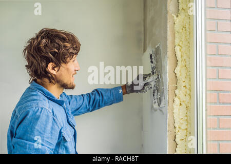 Master ist die Anwendung weiß putty an einer Wand und Verschmieren von Spachtel in einem Zimmer renovieren Haus tagsüber Stockfoto