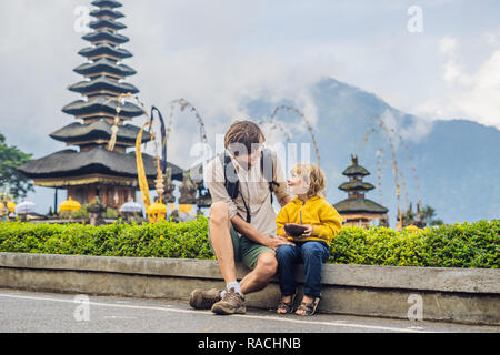 Vater und Sohn im Hintergrund von Pura Ulun Danu Bratan, Bali. Hindu Tempel umgeben von Blumen auf Bratan See, Bali. Große Shivaite wasser Tempel auf Bali, Indonesien. Hindu Tempel. Reisen mit Kindern Konzept BANNER, LANGE FORMAT Stockfoto