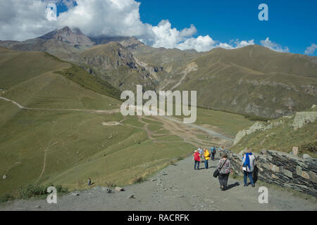 Touristen in der Nähe der Kirche der Heiligen Dreifaltigkeit Gergeti durch den Fluss Chkheri, unter dem Berg Kazbegi im Kaukasus, Georgien, Zentralasien, Asien Stockfoto