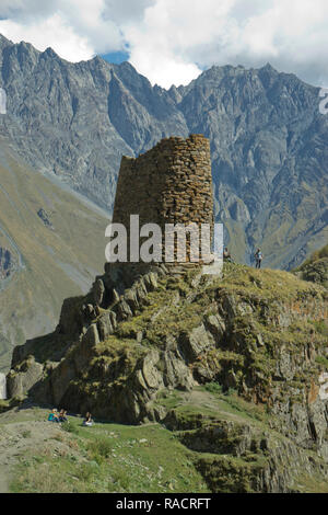 Touristen trekking durch einen Turm in der Nähe der Kirche der Heiligen Dreifaltigkeit Gergeti durch den Fluss Chkheri, unter dem Berg Kazbegi im Kaukasus, Georgien Stockfoto