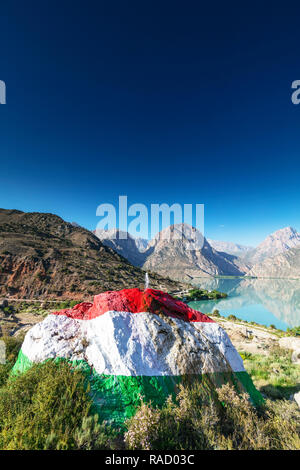 Iskanderkul See mit einem großen Felsen in den Farben der Flagge Tadschikistan im Vordergrund gemalt, Fan Gebirge, Tadschikistan, Zentralasien, Asien Stockfoto