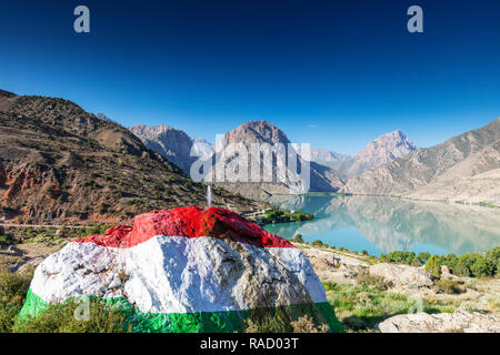 Iskanderkul See mit einem großen Felsen in den Farben der Flagge Tadschikistan im Vordergrund gemalt, Fan Gebirge, Tadschikistan, Zentralasien, Asien Stockfoto