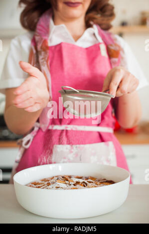 Gießen Zucker Puder auf hausgemachten Apfelkuchen. Hausfrau Köche in der Küche Stockfoto