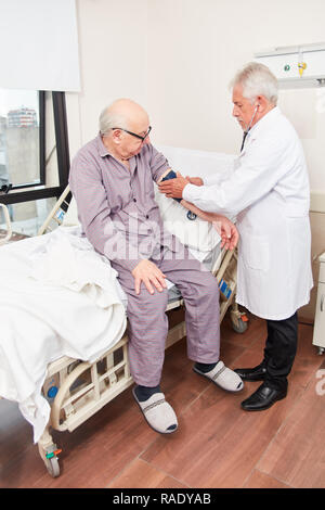 Arzt macht eine Blutdruckmessung in den älteren Mann vorsorglich im Krankenhaus Stockfoto