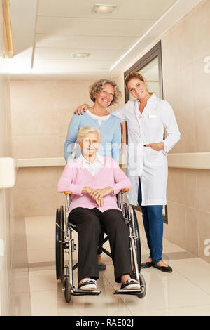 Ärztin mit älteren Frau im Rollstuhl und Tochter im Flur einer Rehabilitationsklinik Stockfoto