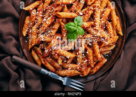 Ein Teil der klassische italienische Penne Arrabiata in einer Schüssel mit Basilikum und frisch geriebener peccorino Käse auf einem alten Holztisch, Ansicht schließen von ab Stockfoto