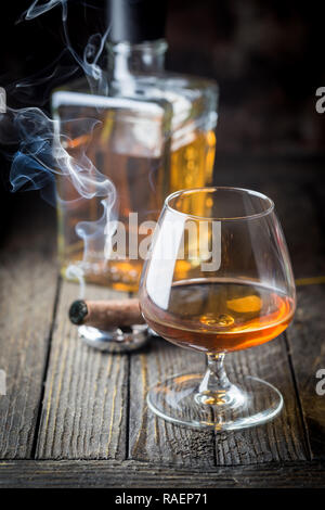 Glas und eine Flasche Weinbrand oder Cognac und Rauchen Zigarre auf dem Holztisch. Stockfoto