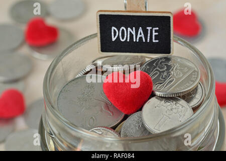 Münzen und Herzen aus Glas Glas mit Label Geld spenden - Nächstenliebe Konzept Stockfoto