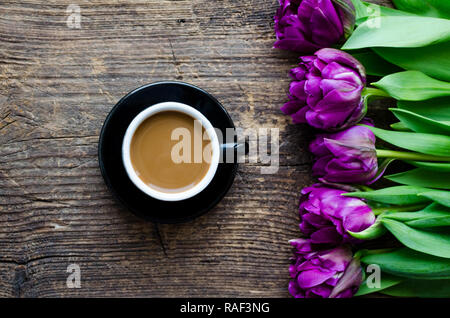 Tasse Kaffee am Morgen und Blumenstrauß der Frühling Blumen Tulpen über rustikal Hintergrund. Ansicht von oben. Morgen Grußkarte. Urlaub, Romantik der Moderne Stockfoto