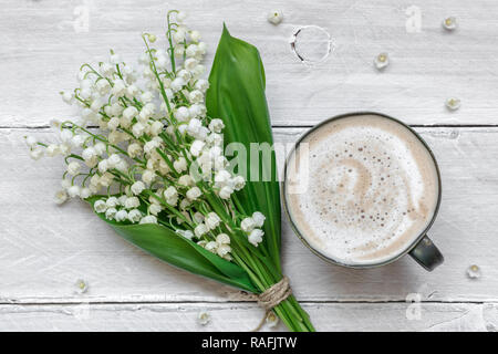 Feder Maiglöckchen blumen blumenstrauss mit Tasse Kaffee mit Milch über weiße Holztisch. valentines oder Tag der Frauen Hintergrund. top View Stockfoto