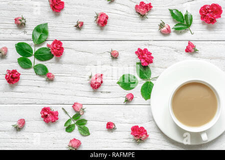 Tasse heißen Cappuccino oder Kaffee mit Milch auf Weiß Untertasse mit Blumen Zusammensetzung aus rosa rosa Blüten mit grünen Blättern. Valentinstag backgr Stockfoto