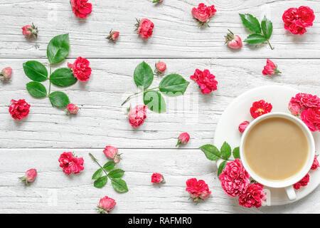 Tasse Cappuccino oder Kaffee mit Milch mit Blumen Zusammensetzung aus rosa rosa Blüten mit grünen Blättern. Valentinstag Hintergrund. Flach, oben Stockfoto