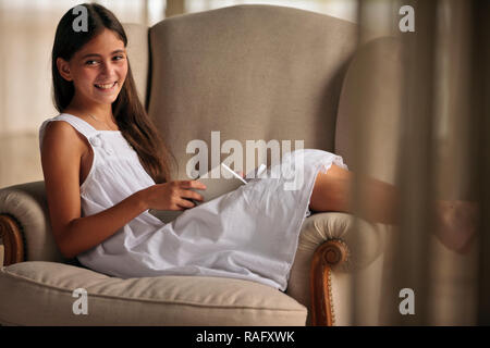Glückliches Mädchen sitzt auf einem Sessel ihr Buch zu lesen. Stockfoto