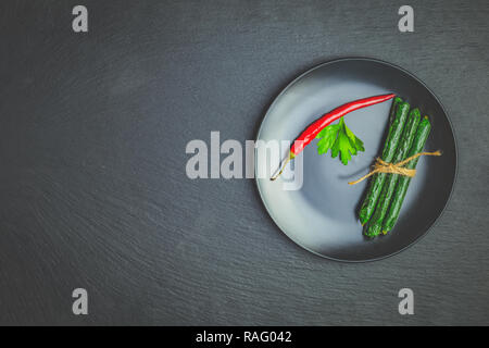 Kabanosy, Würstchen grün mit Wasabi von Schweinefleisch in der Platte auf einem schwarzen Stein Oberfläche mit Zugabe von frischen Kräutern und Gewürzen Stockfoto