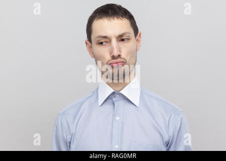 Closeup Portrait von traurig unzufrieden stattlichen Borste Geschäftsmann in klassischem Hellblau Shirt stehen und weg schauen mit Schmollmund Lippen. indoor Studio Stockfoto