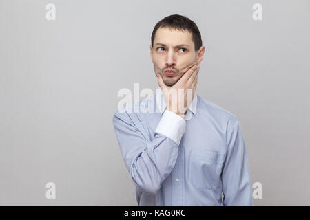 Portrait von nachdenklich stattlichen Borste Geschäftsmann in klassischem Hellblau Shirt stehen, berühren sein Kinn und weg schauen und Denken. indoor Stud Stockfoto