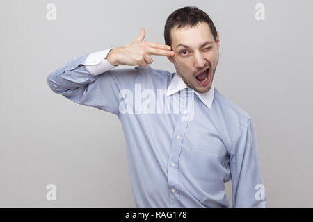 Portrait von Crazy hübscher Borste Geschäftsmann in klassischem Hellblau Shirt mit Pistole Geste und Kamera. indoor Studio shot, iso Stockfoto