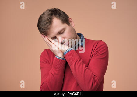 Europäischen Mann in Rot sweaer müde werden über braunen Hintergrund. Stockfoto