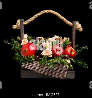 Einzigartiges Geschenk in Form von einer Holzkiste mit Rosen und verschiedene Früchte auf einem schwarzen Hintergrund dargestellt. Ansicht von vorn Stockfoto