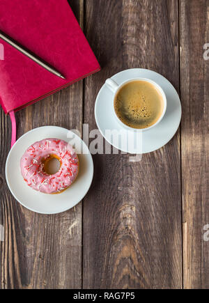 Espresso, Donut mit rosa Zuckerguss und rosa Notepad auf einem rustikalen Holzmöbeln Hintergrund abgedeckt. Ansicht von oben. Stockfoto