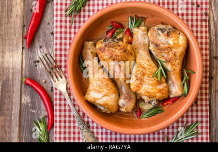 Gebratene Hähnchenschenkel mit Rosmarin, Knoblauch und roter Chili Pfeffer auf rustikalen Holzmöbeln Hintergrund. Ansicht von oben. Stockfoto