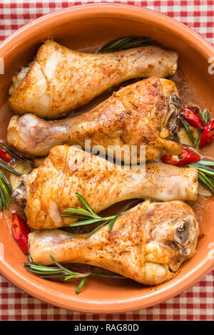 Gebratene Hähnchenschenkel mit Rosmarin, Knoblauch und roter Chili Pfeffer auf rustikalen Holzmöbeln Hintergrund. Ansicht von oben. Stockfoto